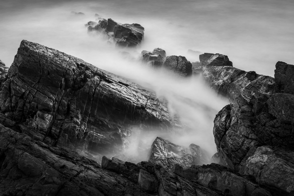 black and white seascape. Submerged rocks form a spiral composition and long exposure turns water into mist. 