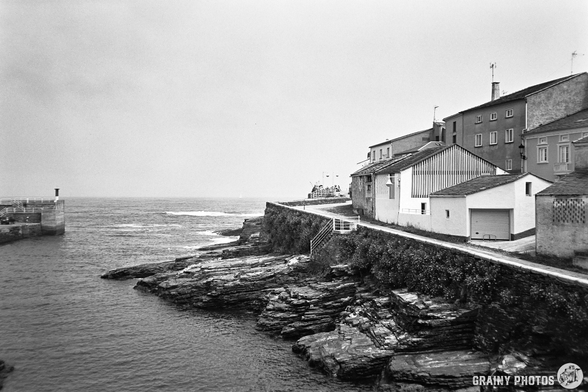 A black-and-white film photo of houses by the coast in Rinlo