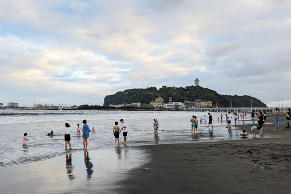 Leute kühlen sich in der Abenddämmerung an einem Strand ab.
Im Hintergrund die Insel Enoshima. 