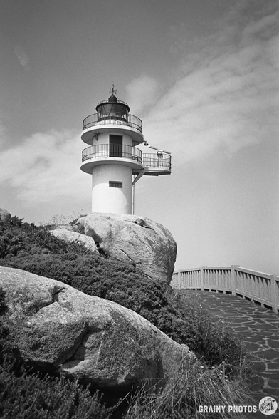 A black-and-white film photo of the Roncadoira lighthouse. A footpath leads to the lighthouse