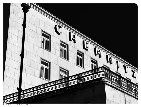 Schwarzweißfotografie: kastenförmiges Hotelgebäude mit eckigem Terassenvorbau, Schriftzug in Großbuchstaben Chemnitzer Hof, von diesem ist nur Chemnitz im Bild zu sehen, dunkles Fallrohr vor sonst hellem Fassadenton, einheitlicher dunkler Himmel darüber