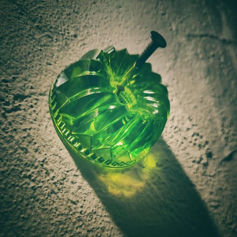 Quadratisches Farbfoto. Es zeigt einen grünen Wackelpudding, der allerdings aus Glas ist und mit einem großen Nagel an die Wand genagelt wurde.