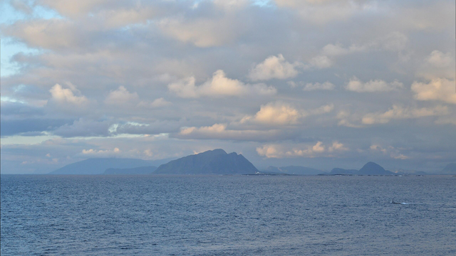 A photo of the Norwegian Sea with mountains in the distance. The sky is filled with clouds.