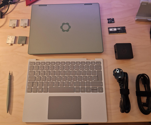 Components of the DIY kit to "build" the framework 12 notebook (closed main body, keyboard, power adapter, RAM, SSD, expansion cards, and a screwdriver matching the color of the computer.