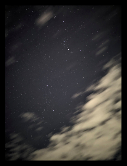 A dark night sky filled with numerous stars, featuring the Orion, Canis Major, and other visible constellations. Streaky, elongated clouds partially obscure the lower and right portions of the sky.