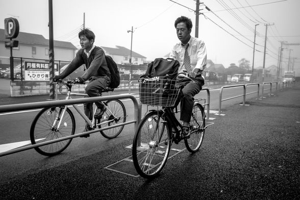 Dos homes muntats en bicicleta van cap a la feina en un dia boirós.