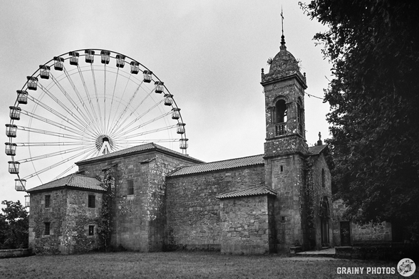 A black-and-white film photo of a church with a Ferris wheel behind it