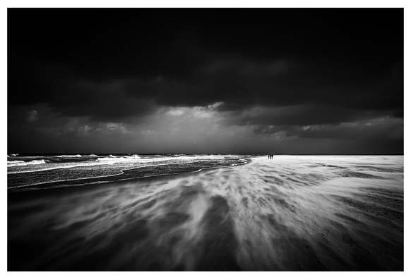 Kontrastreiches Schwarzweiß-Foto: Blick auf einen Stand bei Ouddorp. Oben ein wolkenverhangener Himmel, unten wird Sand durch den Sturm über den Strand gefegt.
