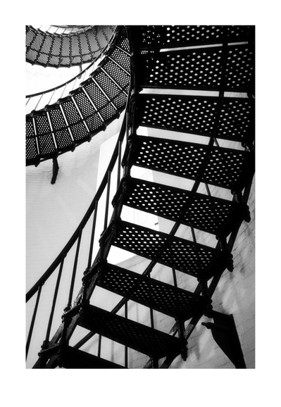 Black and white photo of a spiral staircase with perforated steps ascending into the distance. The image conveys an abstract, geometric feel.