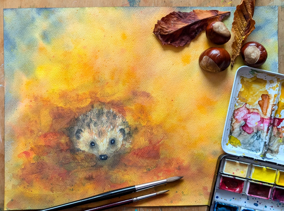 Ein kleiner Igel schaut neugierig aus einem Haufen leuchtend bunter Herbstblätter, die er zum Überwintern zusammengetragen hat. Sein braunes Fell fügt sich harmonisch in die warmen Töne der von der goldenen Herbstsonne beschienenen Umgebung ein. Der Hintergrund besticht durch satte, warme Farben und schafft eine gemütliche Atmosphäre.
Igel im Herbstlaub ist ein handgemaltes Aquarellgemälde der Künstlerin Karen Kaspar.
Hier liegt das Bild auf einem Tisch zusammen mit Pinseln, Aquarellfarben, Herbstlaub und Kastanien.