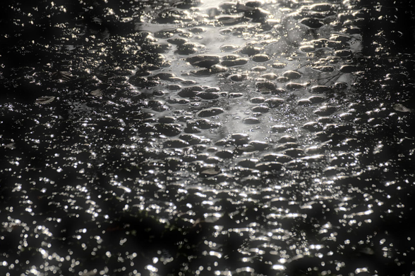 Wasseroberfläche mit Lichtreflexen auf kleinen Wellen und Tropfen