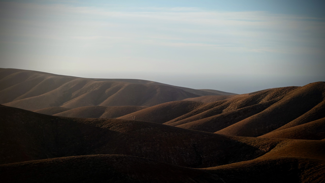 Eine karge wüstenartige Hügellandschaft wird am späten Nachmittag von der tief stehenden Sonne beschienen. Durch die Hänge in der Sonne und die Hänge mit Schatten verstärkt sich das Relief der Berge. 
