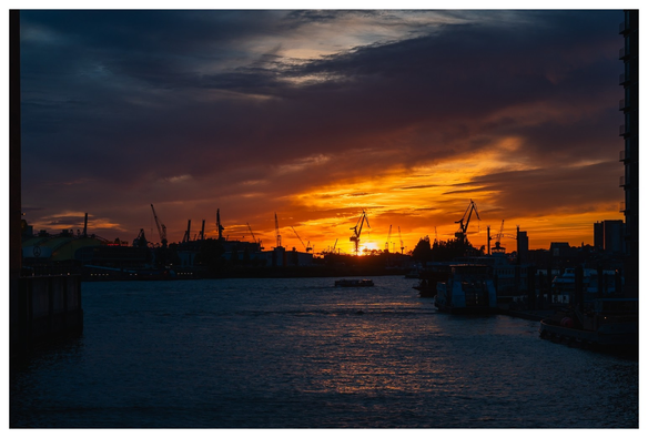 Sonnenuntergang im Hamburger Hafen. Dramatischer Himmel, große Kräne als Silhouetten im Gegenlicht.