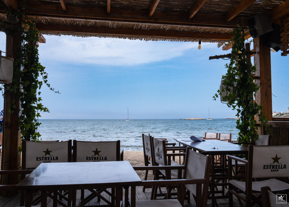 Color photo looking out towards a beach and the sea beyond  from a covered outdoor dining area.