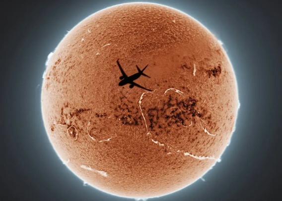 "During a routine time-lapse observation of the solar chromosphere [the thin, reddish layer of the Sun’s atmosphere above the visible surface], I captured a serendipitous moment when an aircraft crossed the field of view. Preserving this transient frame, I employed multiple blending modes to enhance the details of the solar background. Beyond stacking individual video frames, I processed the sequence, undertook colour inversion and synthesised 100 images through combined mean and minimum blending. This dual approach effectively accentuated both bright plages [active regions in the chromosphere] and dark laments through enhanced contrast.

"The composite image reveals the evolution of the Sun’s dynamic surface across a two-hour observational period, while the aircraft’s two-second transit remains frozen in time. This layered imaging rearranges time, blending celestial bodies and human technology in one photo."