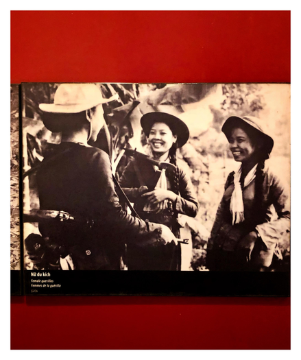 A historical black and white photograph mounted on a red wall at the Vietnamese Women’s Museum. Three female guerrilla soldiers in hats and scarves, carrying rifles, stand outdoors amid indistinct surroundings and share a moment of laughter. I’m sure these photos were used for morale-boosting propaganda (as all sides do in war), but I’m still struck by the apparently sincere lighthearted moment this image seems to capture.

Museum text below the photo reads: Nữ du kích
Female guerillas
Femmes de la guérilla
Củ Chí

(Củ Chí is a district in Southern Vietnam where the photo was taken.)