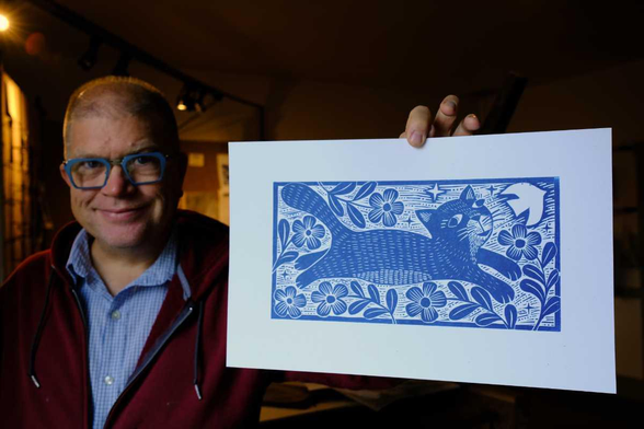 artist holding a panoramic woodcut with a cat in flowers design