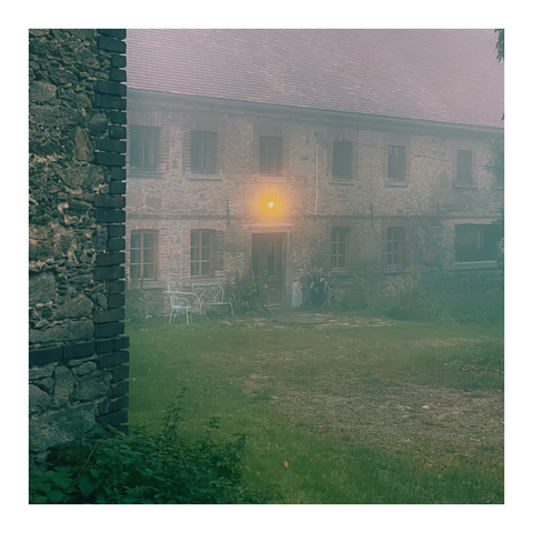Blick an einer Hauskante vorbei ein anderes Bauernhaus mit Nebel. Über der Haustür leuchtet gelb eine Lampe
