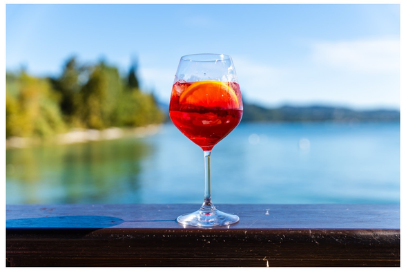 Rotes Getränk mit Eis in Weinglas vor See.