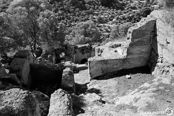 Ancient stone ruins of the abandoned Castillejo rise on a rocky hillside near Guájar-Faragüit, with weathered walls surrounded by scattered trees and dense vegetation under sunlight.