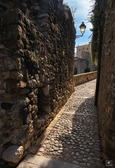 Color photo of a narrow cobblestone passageway between rough stone walls.