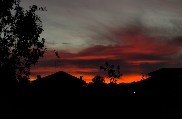 picture of a sunset with the sky and clouds in bright orange colours. In the foreground the silhouette of some houses