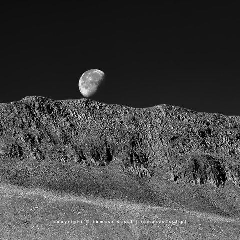 Captured just above the crest, the moon appears to be rolling over the edge.