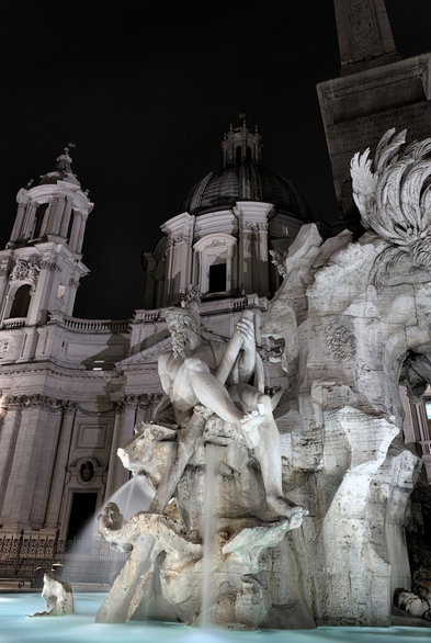 Fotografía nocturna de un detalle de la fuente de los cuatro rios de en la plaza Navona de Roma. Tras la fuente se ve la fschada de la iglesia de santa ines en agonia.
