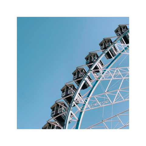 detail shot of parts of a huge ferris wheel against the blue sky. the cabins actually look like tiny houses with gabled roofs