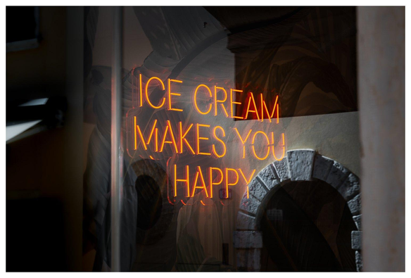 Schriftzug "ICE CREAM MAKES YOU HAPPY" in einem Schaufenster einer Gelateria. Im Schafenster spiegelt sich italienischer Krimskrams wie italienische Häuser und ein italienischer Torbogen. 
