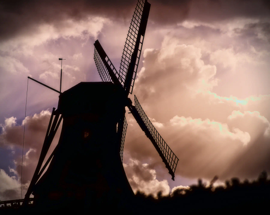 Die Silhouette einer alten Galerie-Windmühle hebt sich vom bewölkten Himmel ab. Von rechts scheint durch die Lücken in den Wolken goldenes Sonnenlicht und taucht den Himmel in goldene und violette Töne. Das ganze Bild wirkt dadurch geradezu unwirklich. Nur wenige Augenblicke, nachdem das Bild aufgenommen wurde, fing es ziemlich heftig an zu regnen.