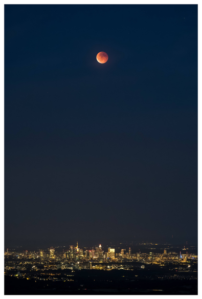 A vertically taken photo showing the blood moon over Frankfurt's illuminated skyline.