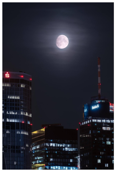 The almost full moon is framed by three skyscrapes.