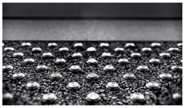 Eine vielzahl im Grid angeordneter Metallischer Nupsies auf Asphalt, die sehbehinderten Menschen Orientierung bieten sollen.