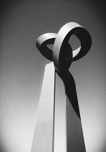 A black and white photo showing a low angle view of a sculpture, a single steel bar twisted and intertwined into a knot.