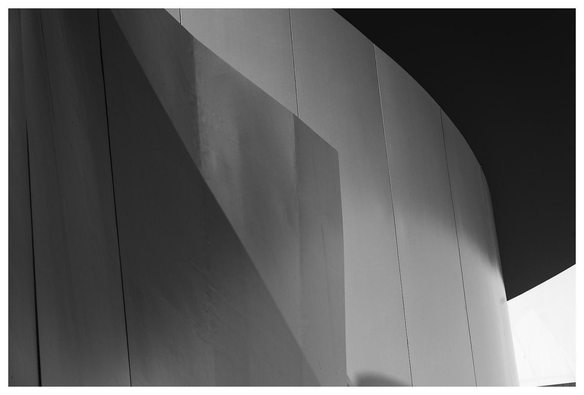 Schwart/Weiß-Bild einer geschwungenen Aluminium-Außenhaut eines Museums im direkten Sonnenlicht. Dahinter ein schwarz erscheinender Himmel.