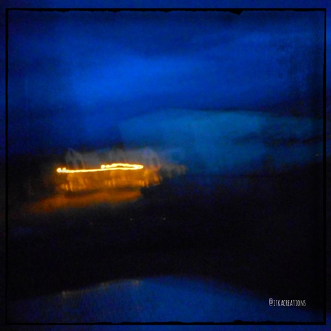 Photo à la limite de l'abstraction : ciel d'encre bleue, la nuit. Au loin, on aperçoit une maison. Le "bougé" de la photo laisse une trace lumineuse de l'éclairage public.