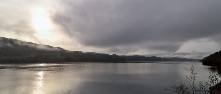 Vue sur le Loch Ness, la lumière est pâle et des nappe de brumes couvrent le relief de l’autre côté du lac