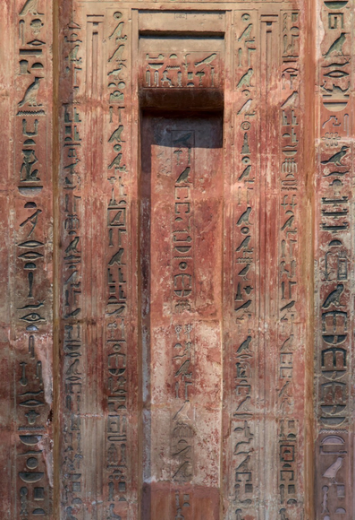Photo de face d’une fausse porte égyptienne en pierre ocre, pleine de hiéroglyphes gravés