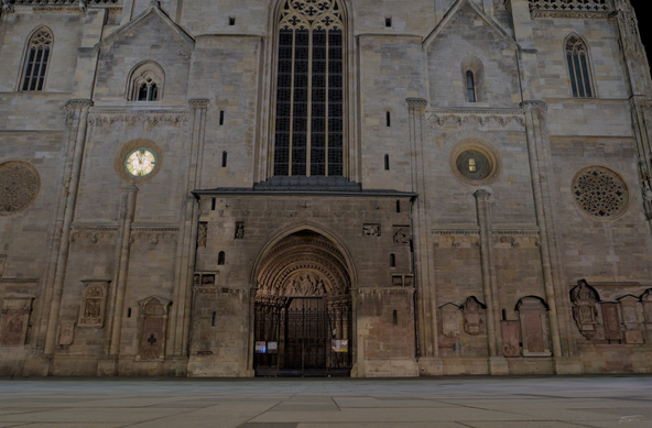 Das Foto zeigt das sogenannte Riesentor, den prächtigen Haupteingang des Stephansdoms in Wien, bei Nacht. Die Fassade des gotischen Bauwerks ist mit Steinreliefs und fein gearbeiteten Details verziert. Über dem mittigen Spitzbogenportal erhebt sich ein großes gotisches Fenster. Die Szene ist ruhig, die Beleuchtung betont die architektonischen Strukturen und lässt die imposante Größe des Portals und der umgebenden Mauern deutlich werden.