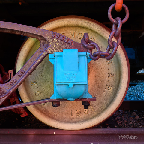 A photo of a wheel and other appurtenances of a steam locomotive built in 1896 by Baldwin Locomotive Works and retired in 1963.  It now functions as a teaching tool with its left side painted in traditional black while the right side is color coded to highlight a feature or group of features that make up the total engine.