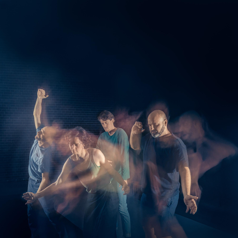 an artistic photo taken for my partner's event "Dancing Meditation". a dark blue image shows four people dancing in long exposure leaving streaks of colour and faint figures
