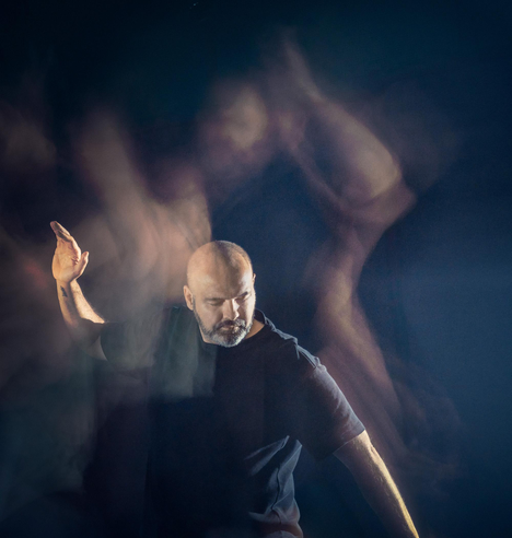 an artistic photo taken for my partner's event "Dancing Meditation". a dark blue image shows a man dancing in long exposure leaving streaks of colour and faint figures