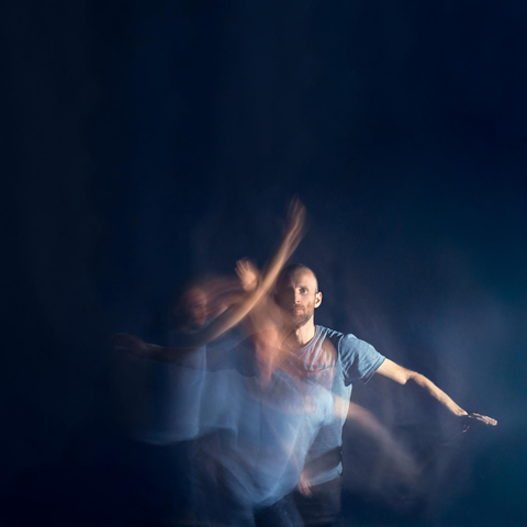 an artistic photo taken for my partner's event "Dancing Meditation". a dark blue image shows a man dancing in long exposure leaving streaks of colour and faint figures