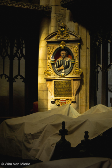 A brightly coloured effigy in the corner of the choir captured in the light. The stalls are covered in sheets to protect them from dust.