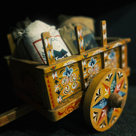 Small, fake bags of coffee fill a wooden tabletop cart resting on the floor.
