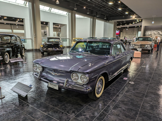 A wideshot of a car museum floor with a 1960 us car in purple in the middle