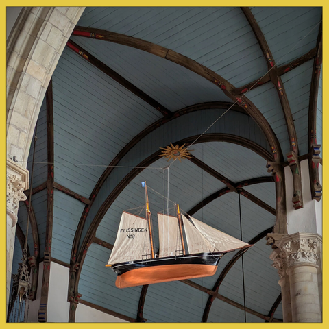 scale model of a fishing boat with sail, with the background of the blue-gray painted ceiling of a church