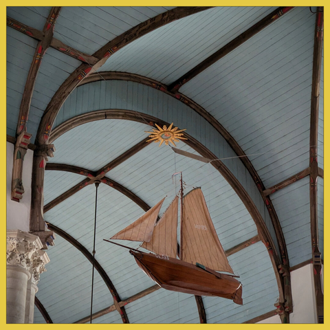 scale model of a fishing boat with sail, with the background of the blue-gray painted ceiling of a church