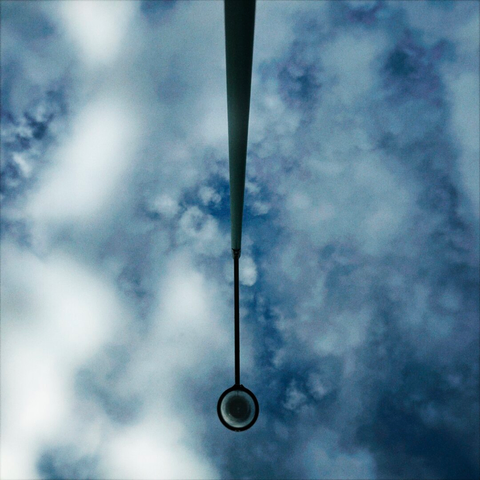 A street light viewed from directly below dips down into frame under a white and blue partly cloudy sky.